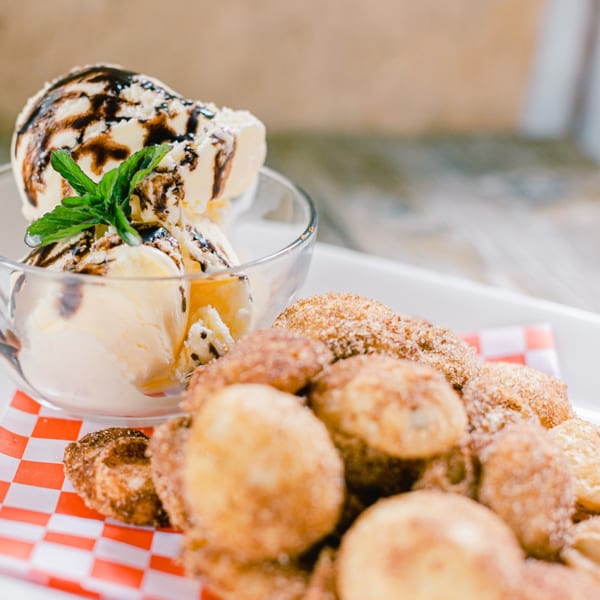 Mexican dessert with vanilla ice cream topped with chocolate syrup and mint, next to churro bites.
