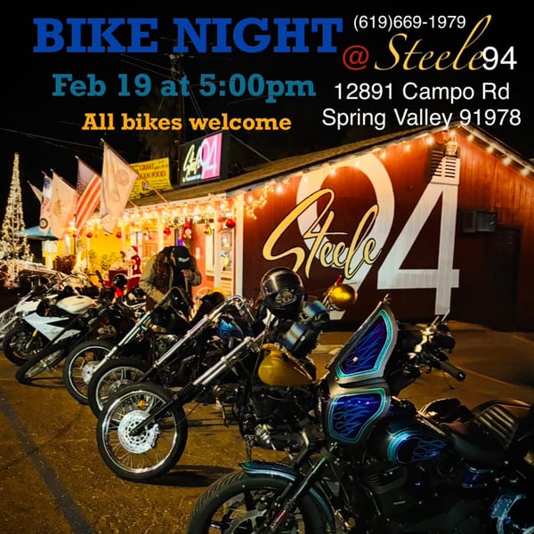 Motorcycles parked outside Steele 94 Restaurant Bar at night, with festive lights and a person.