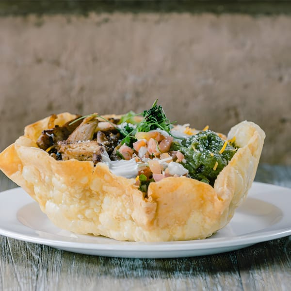 A crispy taco salad bowl filled with grilled chicken, guacamole, pico de gallo, and sour cream.