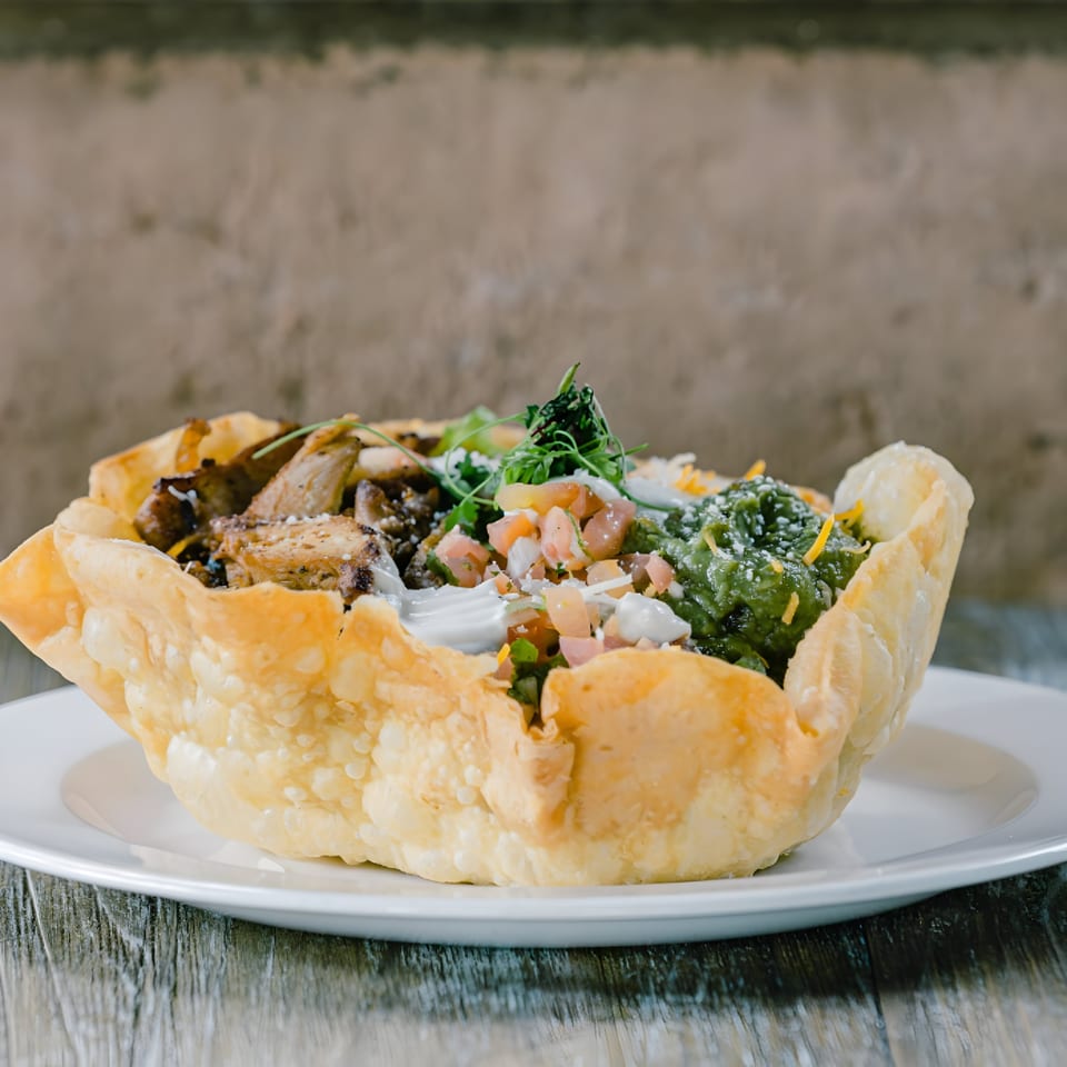 A crispy taco salad bowl filled with grilled chicken, guacamole, pico de gallo, and sour cream.