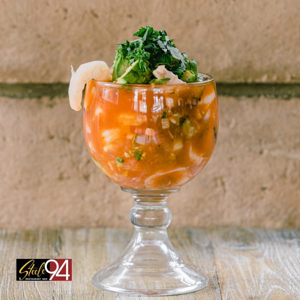 A Mexican shrimp cocktail in a goblet, garnished with avocado, cilantro, and a shrimp.