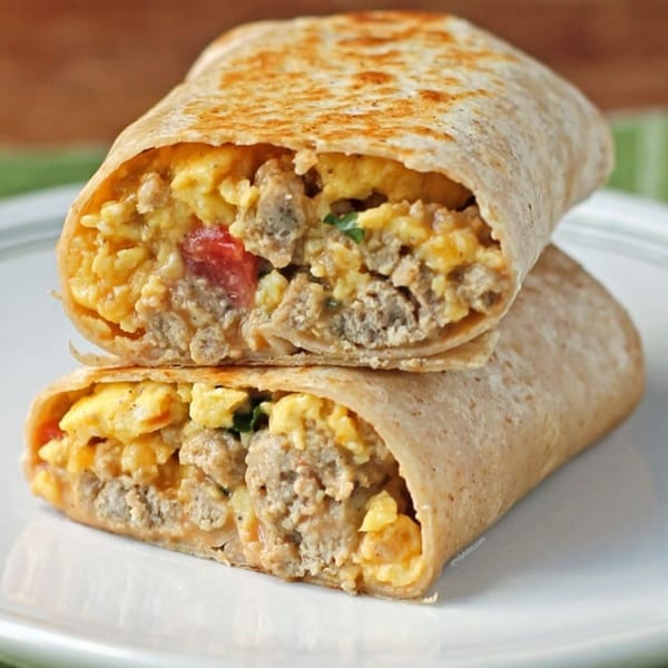 Two halves of a breakfast burrito filled with scrambled eggs, sausage, and diced tomatoes.